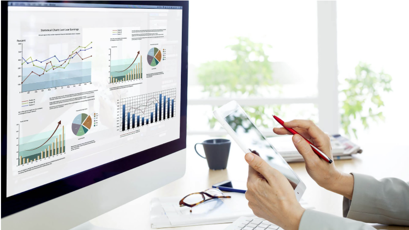 A person at a Melbourne web design agency holds a tablet and pen, studying a computer screen filled with various charts and graphs. A coffee cup rests on the desk, while the background reveals a bright room adorned with plants. | Ven Agency